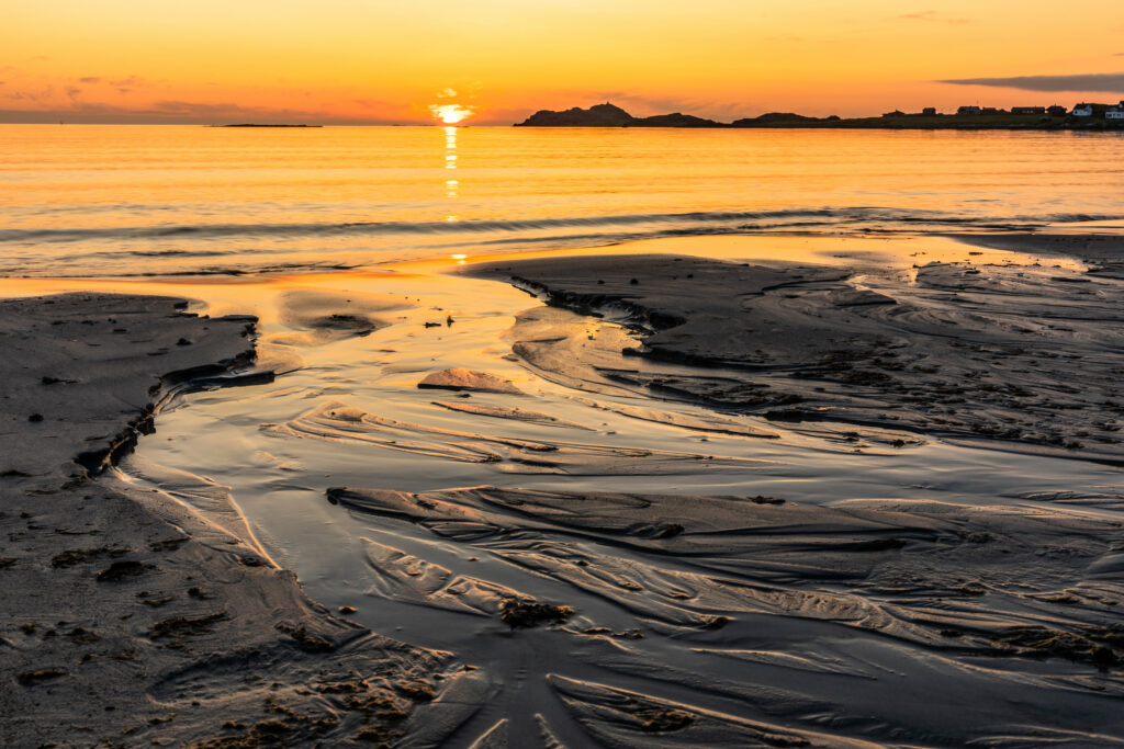 Golden sunset over calm sea rugged coastline smooth rippled sand and tide pools wallpaper background