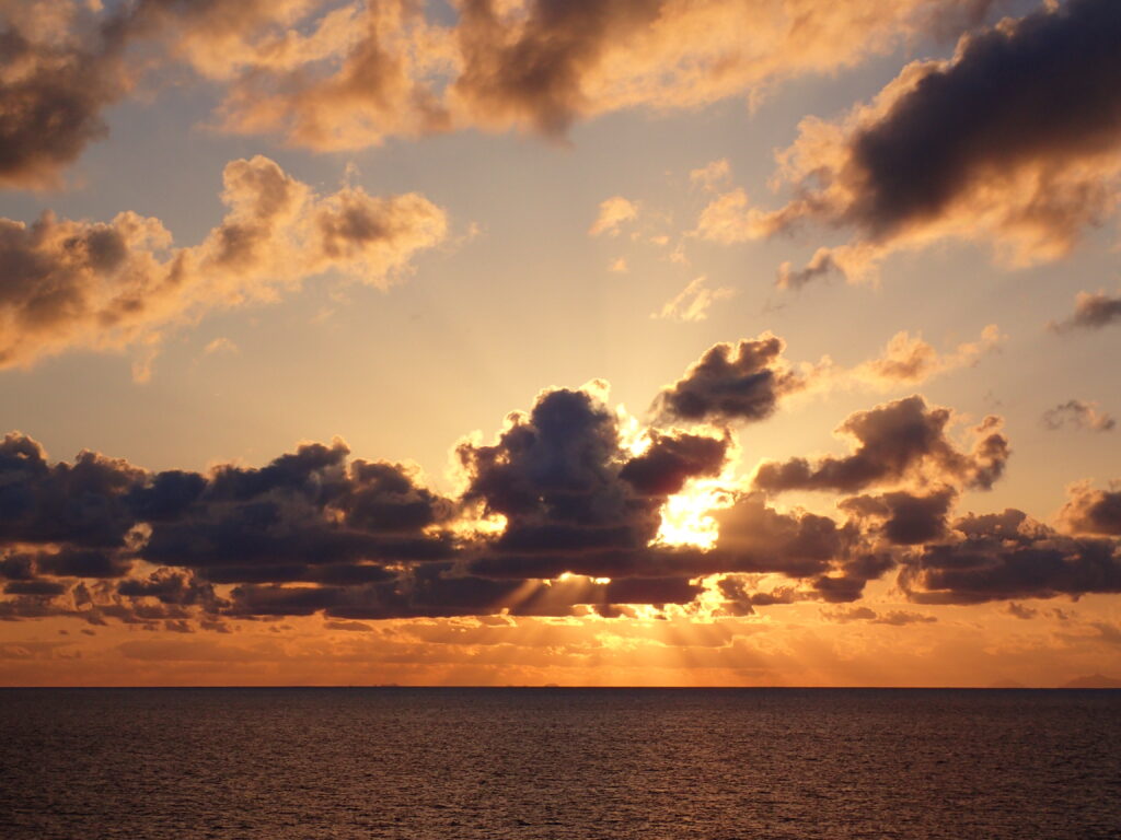 Golden sunlight through clouds over calm sea at sunset with warm orange and blue tones wallpaper