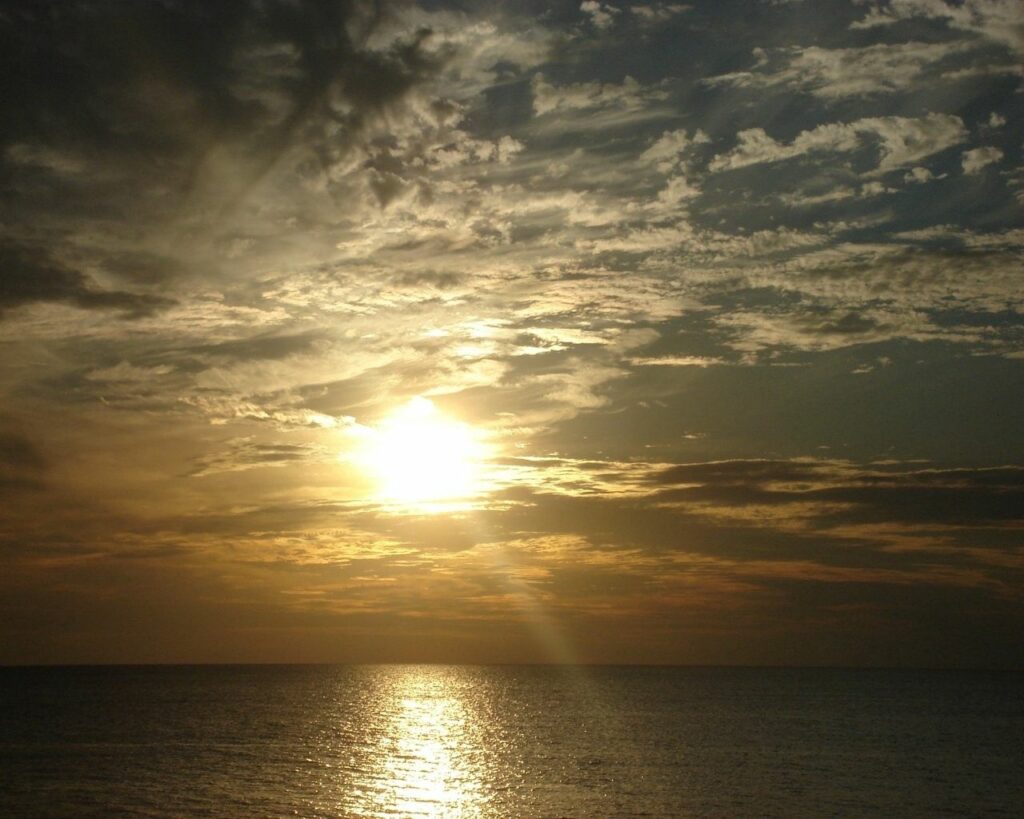Breathtaking sunset over calm sea with golden light beams and glowing clouds reflection wallpaper