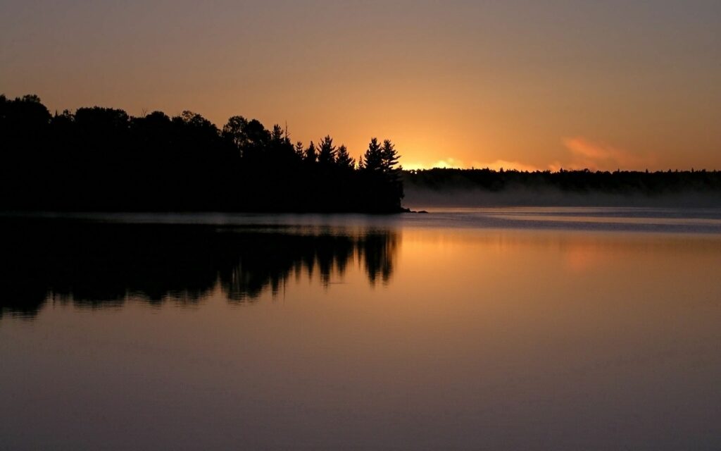 Sunset over calm water with golden glow trees coast reflection and peaceful misty evening wallpaper
