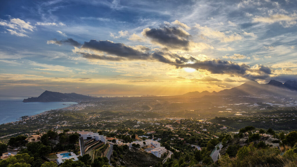 Aerial view of coastal city with lush trees under dramatic sunset and warm golden sunlight Wallpaper