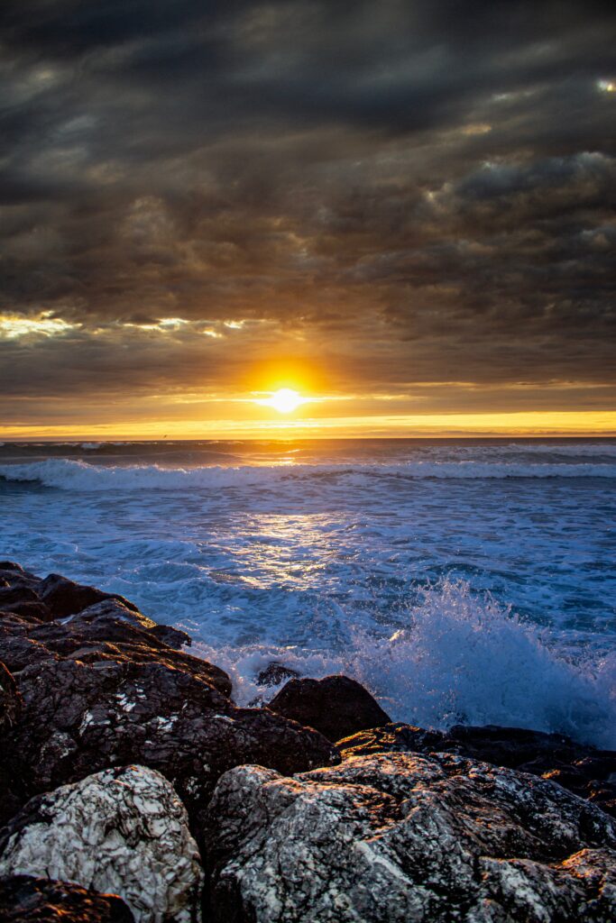 Sunset over crashing waves and rugged rocks illuminated by golden sunlight and vibrant sky Wallpaper