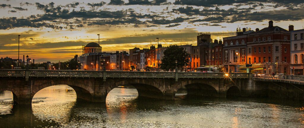 Sunset over Dublin skyline golden glow on historic bridge reflecting on calm river wallpaper