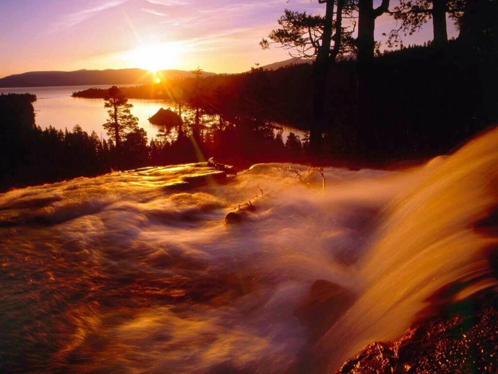 Radiant sunset over flowing stream and cascading falls with tree silhouettes and peaceful horizon Wallpaper