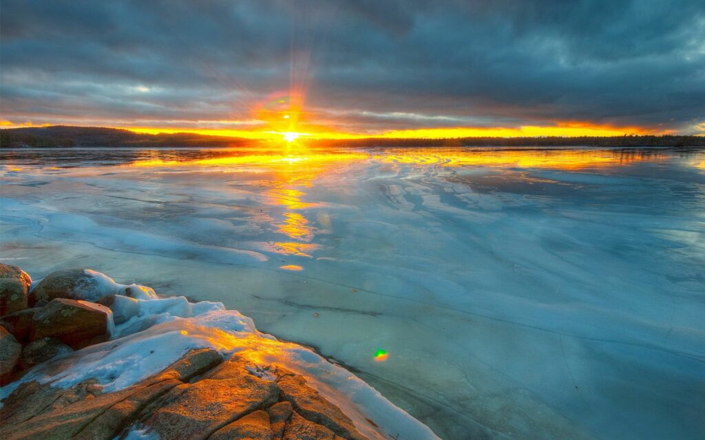 Frozen river at sunset with golden reflections and frosted stones in a serene winter landscape Wallpaper