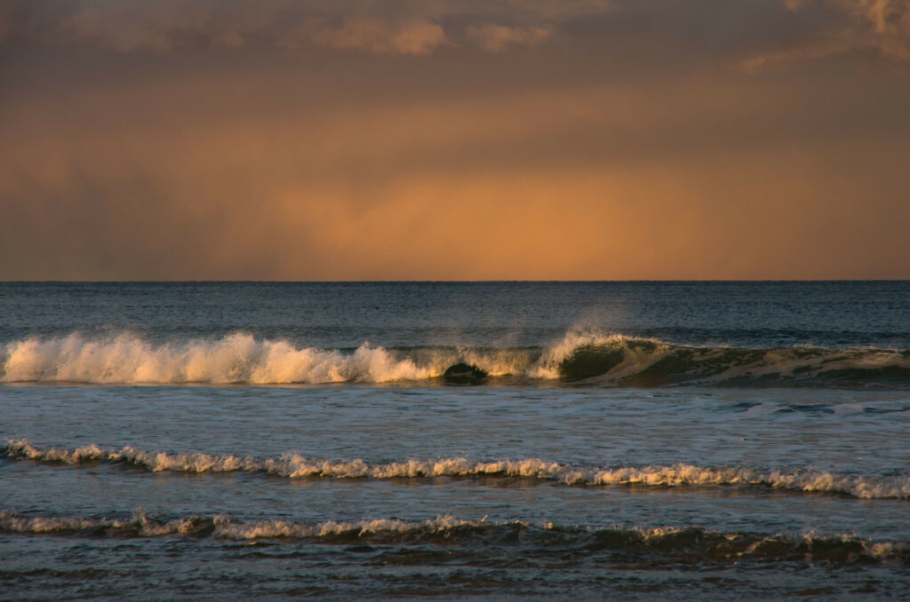 Golden sunlight over gentle waves meets deep blue sea and warm sunset hues on horizon Wallpaper