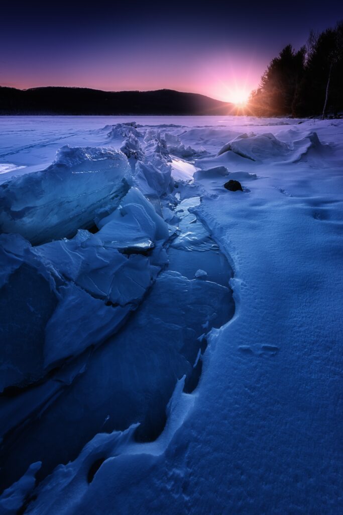 Winter sunset over jagged ice and pristine snow on a frozen lake with deep blue hues background Wallpaper