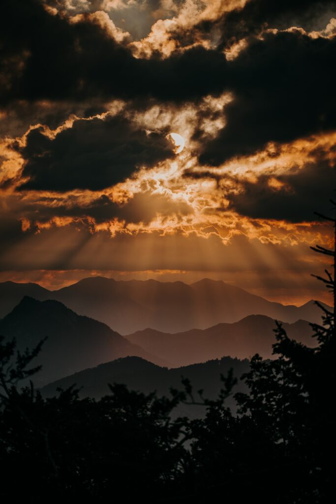 Golden sunlight breaks through dramatic clouds over layered mountain peaks at sunset landscape Wallpaper