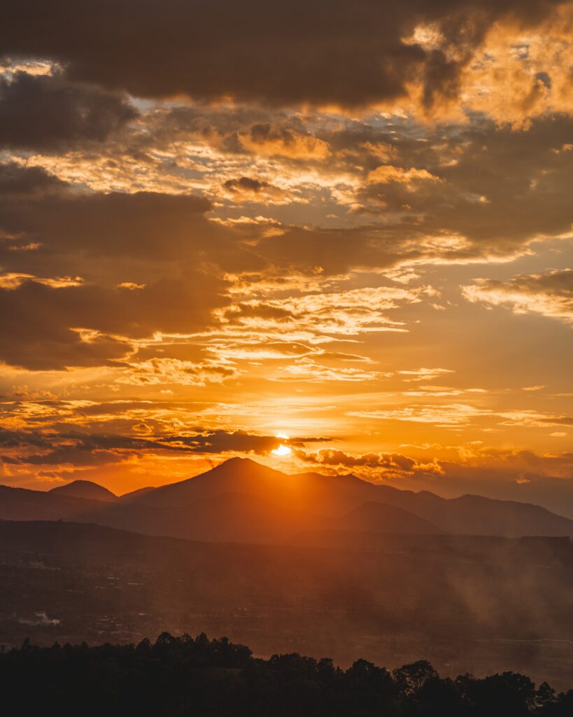 Sunset wallpaper with golden sky over layered mountains and shadowy forest in warm vibrant tones