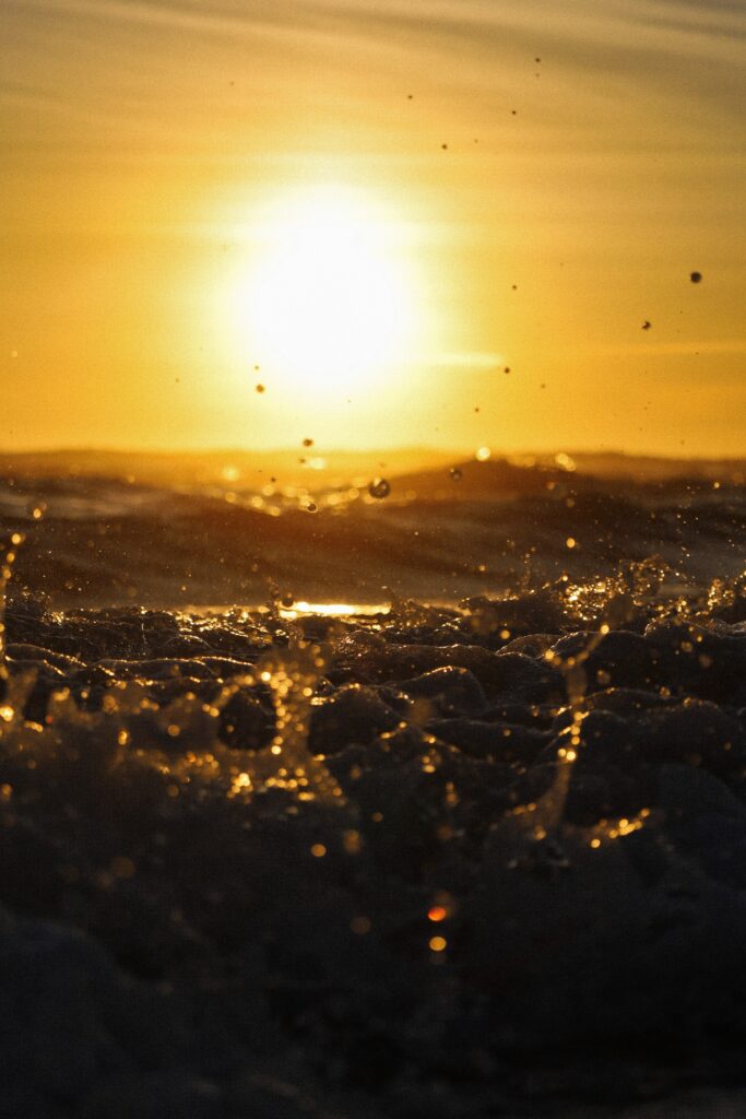 Vibrant golden sunset over ocean waves crashing with shimmering water sprays dynamic seascape wallpaper