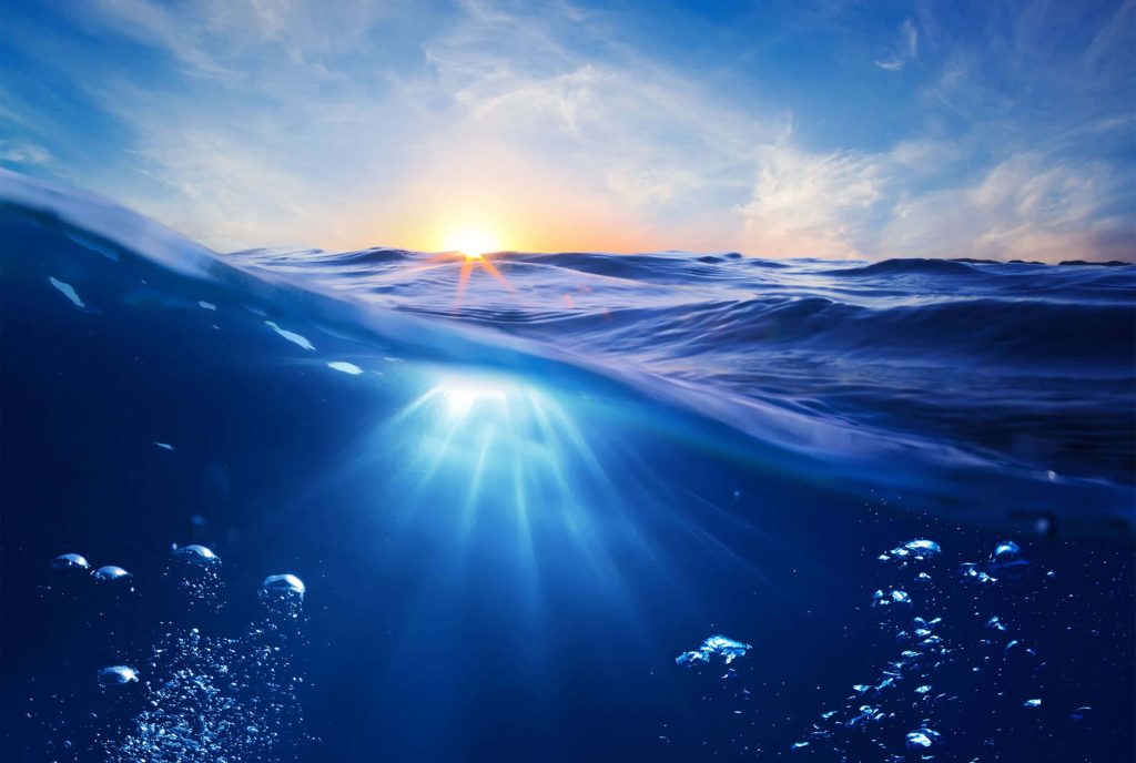 Glowing golden sunset over ocean with light rays illuminating rising air bubbles underwater Wallpaper