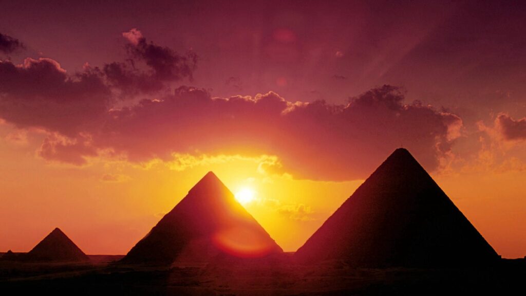 Majestic sunset over iconic Egyptian pyramids with golden light and vibrant orange purple sky Wallpaper