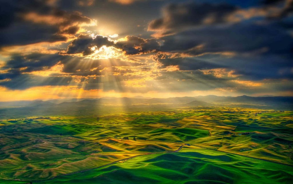 Palouse landscape with rolling green hills and golden sunbeams piercing dramatic sunset clouds Wallpaper