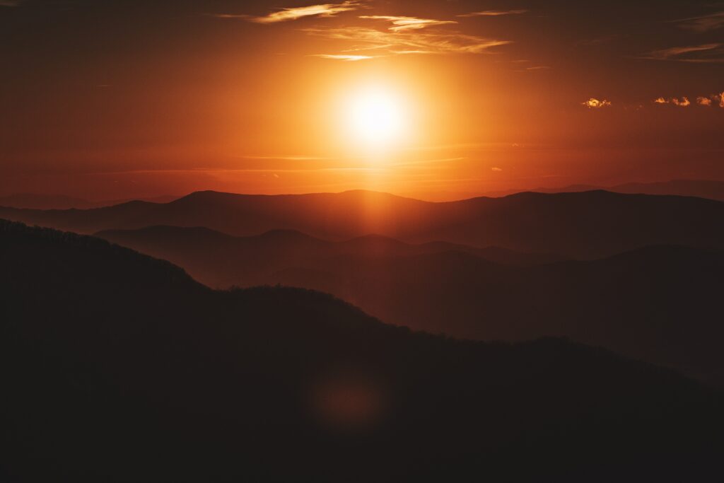 Sunset over rolling dark hills with warm golden orange sky creating serene landscape wallpaper