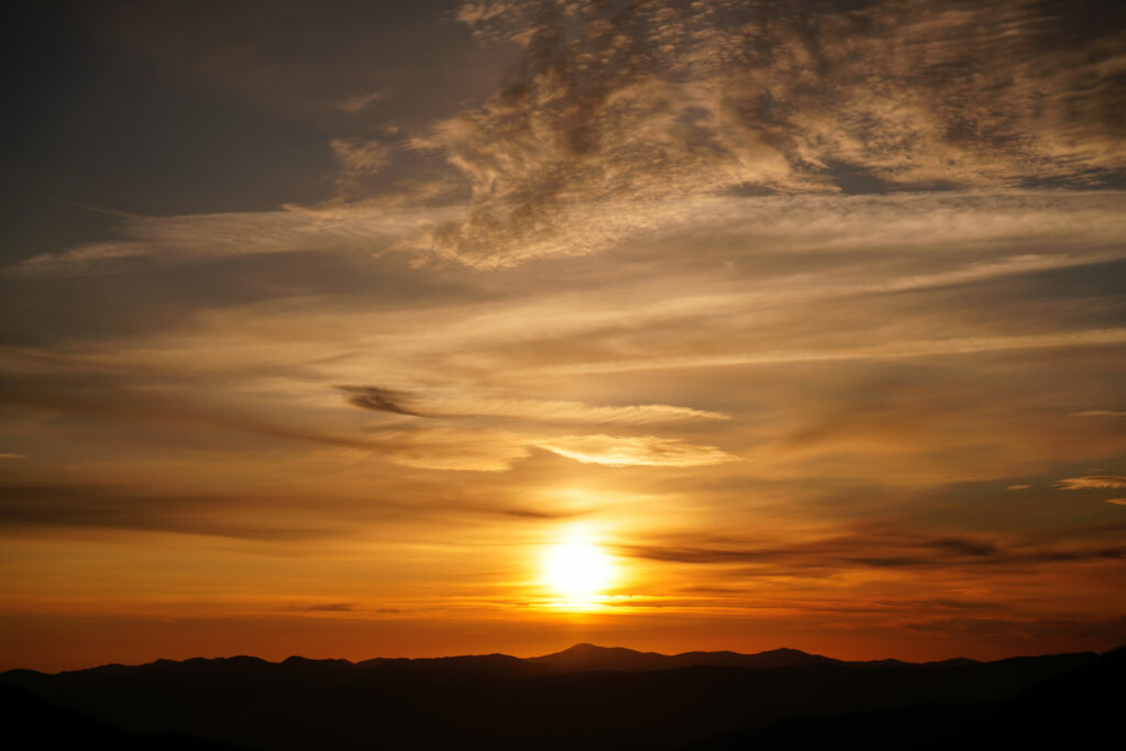 Vibrant golden sun setting behind rolling hills with fiery orange sky and dramatic clouds wallpaper