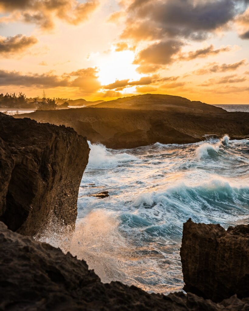 Sunset golden light on rugged coastal rocks with crashing waves and dynamic ocean motion Wallpaper