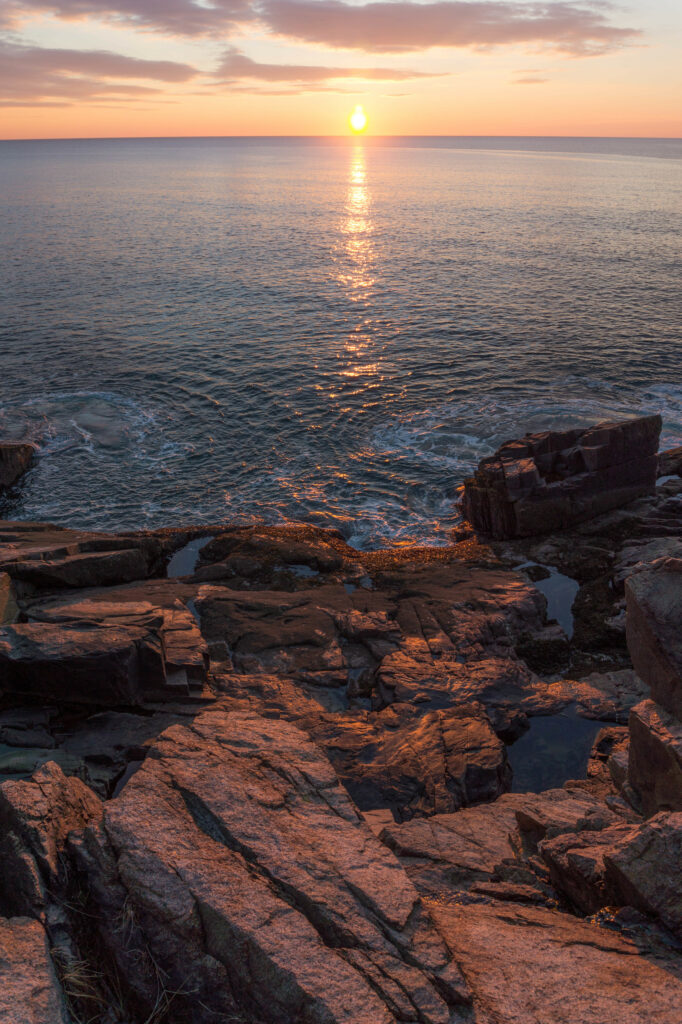 Sunset over rugged cliffs and calm sea with golden sunlight reflecting on rocky coast wallpaper