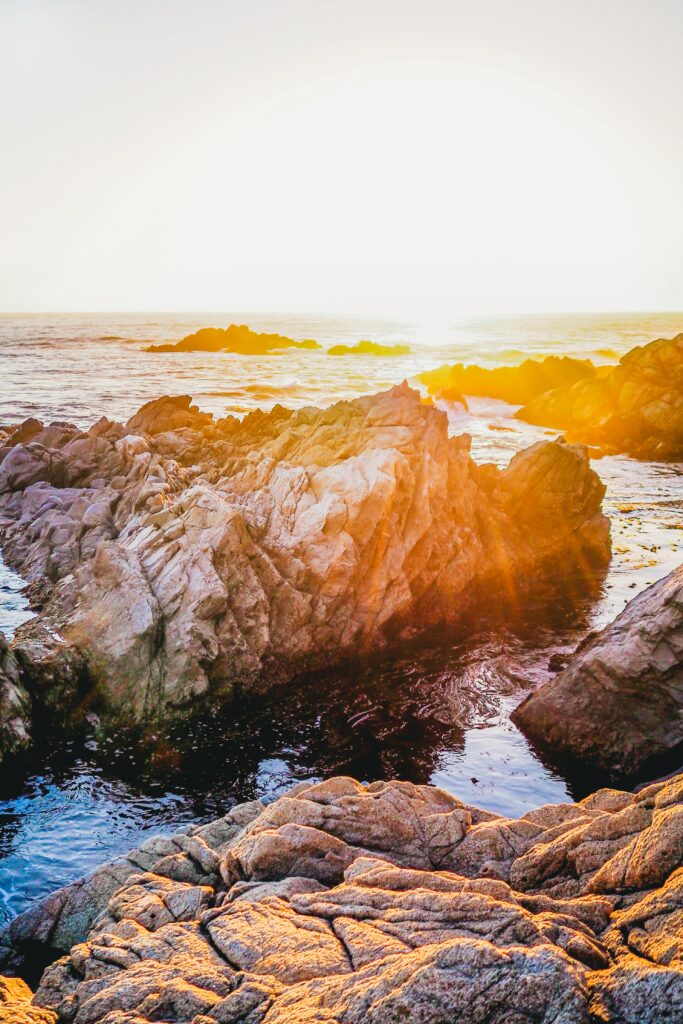 Rugged coastal rocks bathed in golden sunset light with calm shimmering sea and warm tones Wallpaper