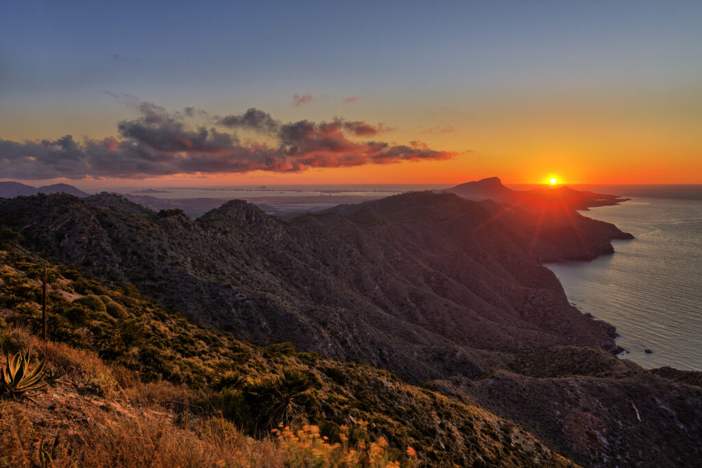 Sunset over rugged island mountains descending to sea with vibrant orange and purple sky wallpaper