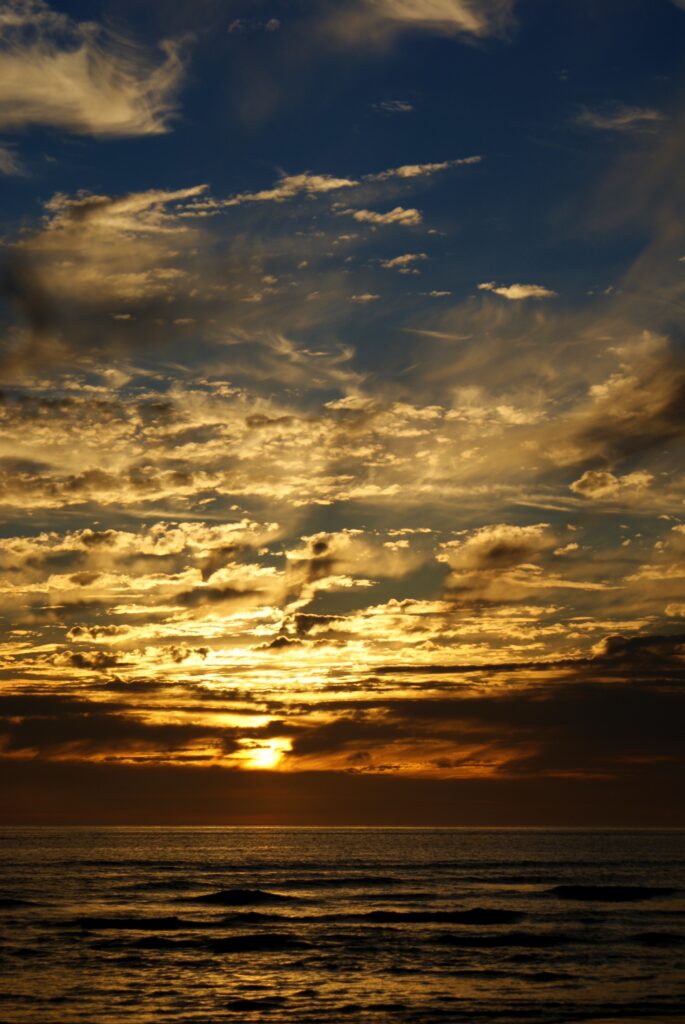Breathtaking sunset over sea with golden light reflecting on waves and dramatic colorful clouds Wallpaper