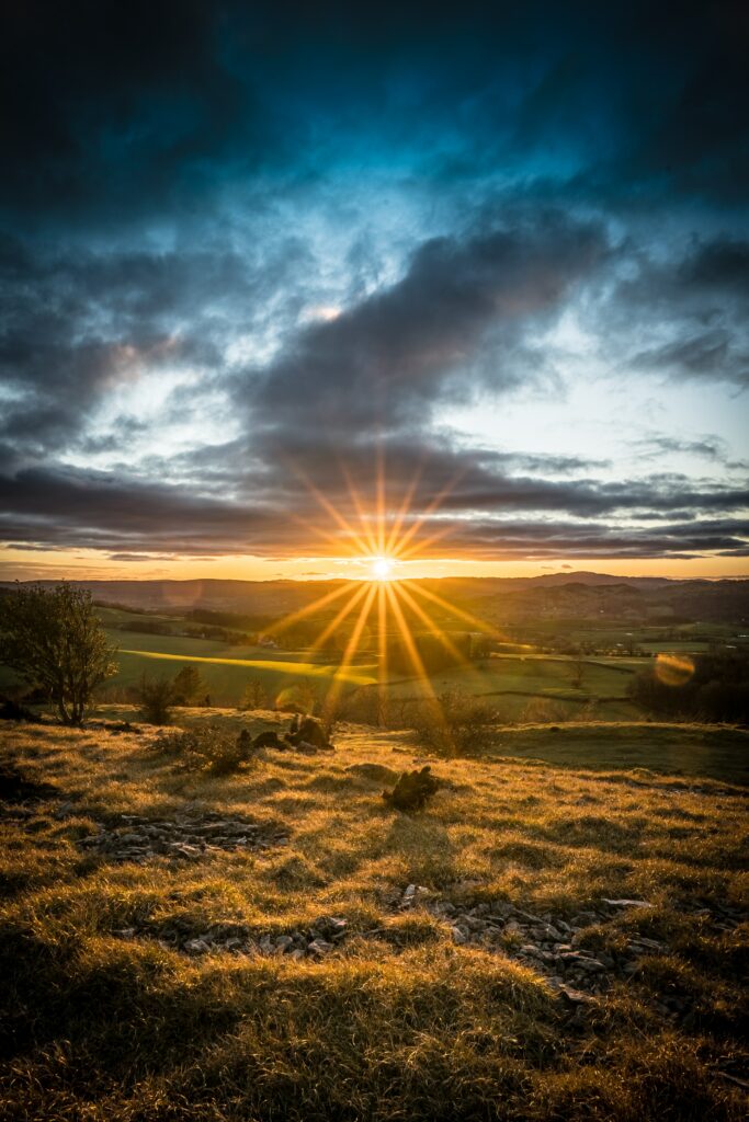 Sunset over serene rolling field with golden light and dramatic vibrant fiery orange sky Wallpaper