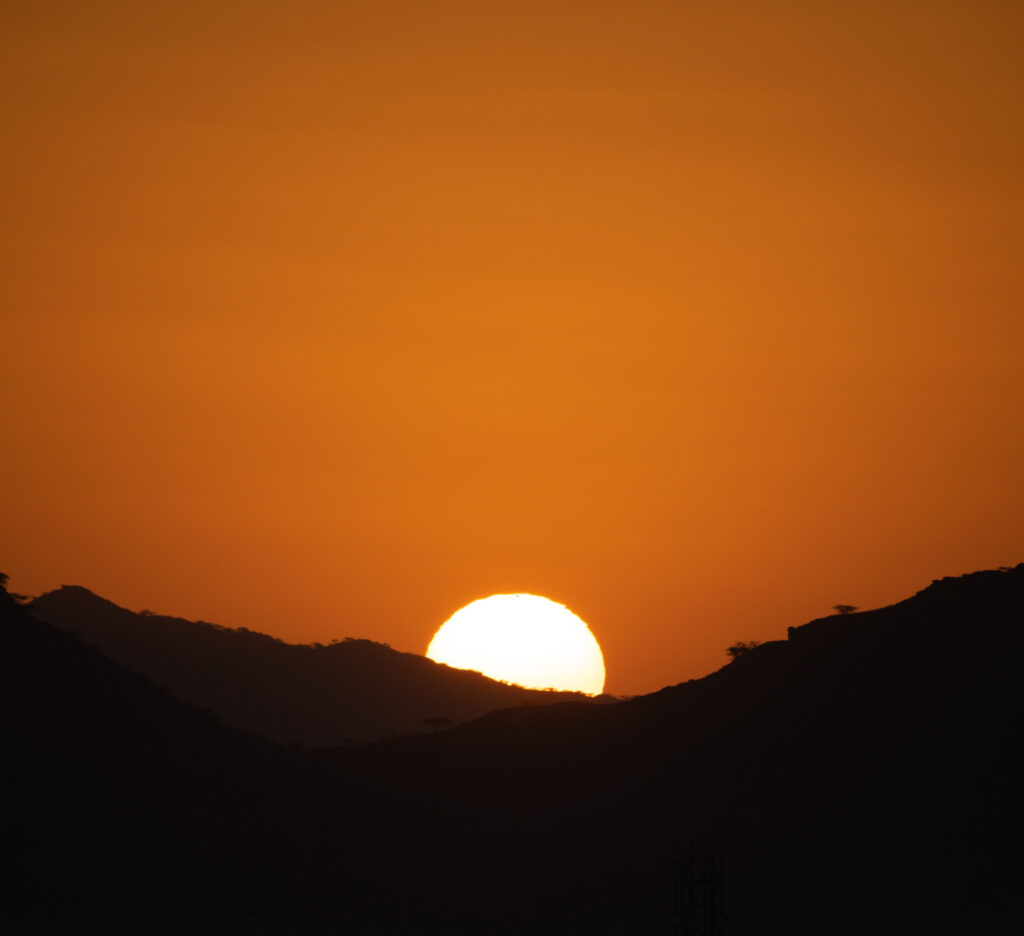 Sunset wallpaper with glowing sun behind dark mountains casting warm orange and gold hues