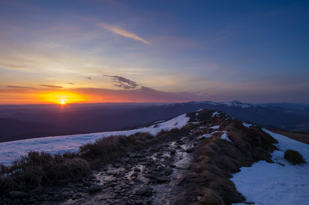 Sunset over snow-dusted mountain path with golden light and vivid orange and blue sky Wallpaper