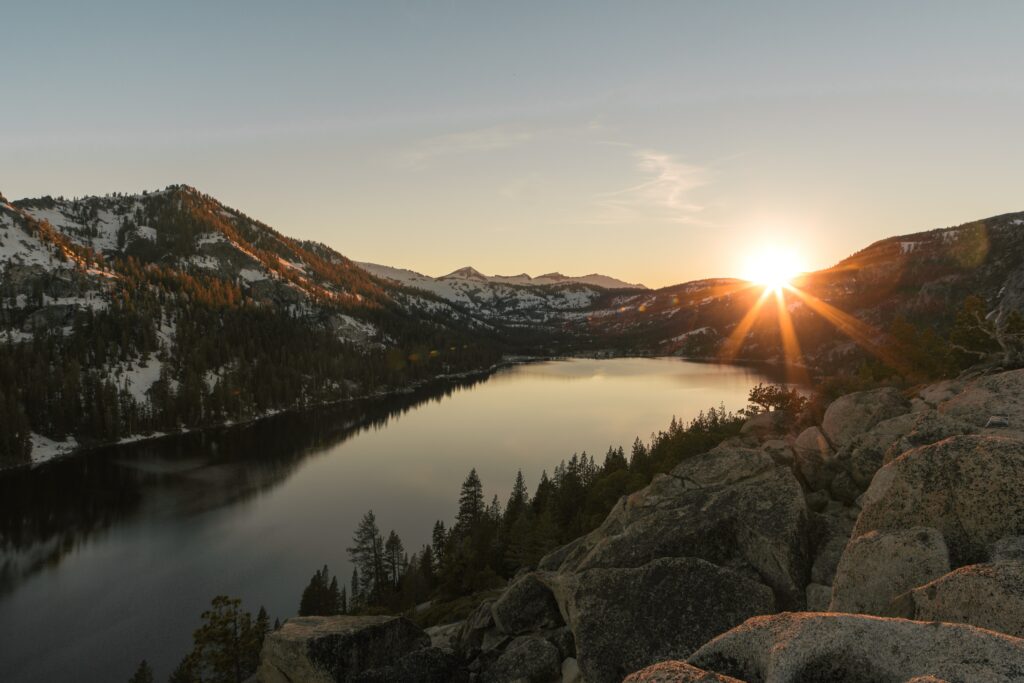 Sunset over tranquil lake with snow-capped mountains and rugged stones serene landscape wallpaper
