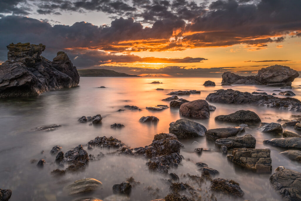 Tranquil bay sunset wallpaper with golden light calm waters rugged shore and dramatic clouds