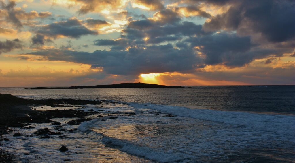 Breathtaking sunset over gentle ocean waves with golden orange sky and dramatic clouds wallpaper