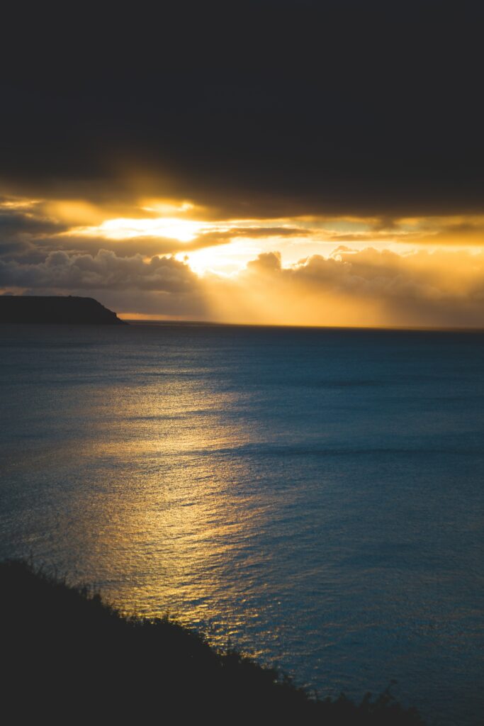 Golden sunset with sunbeams breaking through clouds over calm deep blue sea coastal scene Wallpaper