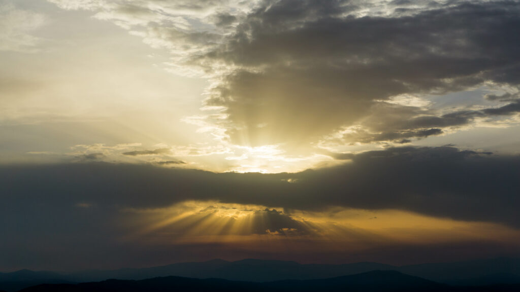 Breathtaking sunset wallpaper with golden rays through dramatic clouds over serene landscape