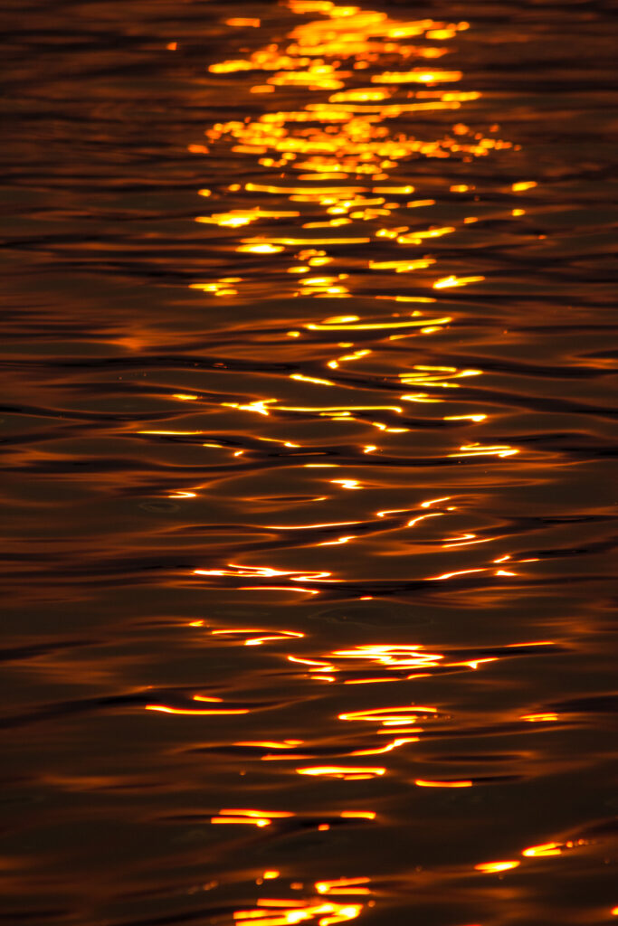 Sunset golden light reflecting on gentle water ripples in a tranquil vibrant orange wallpaper background