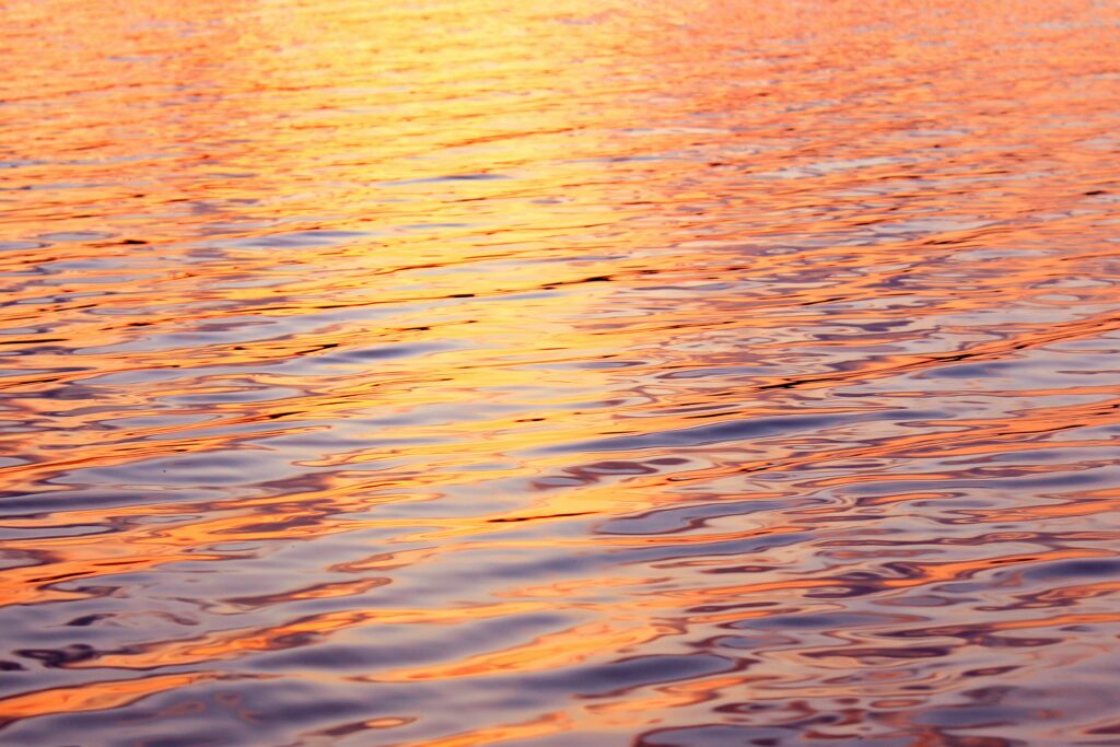 Sunset over tranquil water with golden ripples and soft waves creating serene glare wallpaper