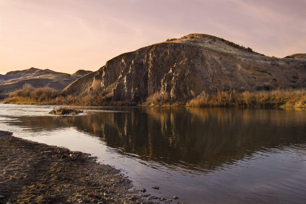 Tranquil river beside rugged rocky coast with hill under golden sunset sky natural landscape Wallpaper