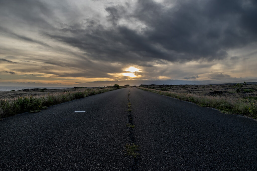 Empty road through open fields at sunset under dramatic rolling clouds serene nature wallpaper