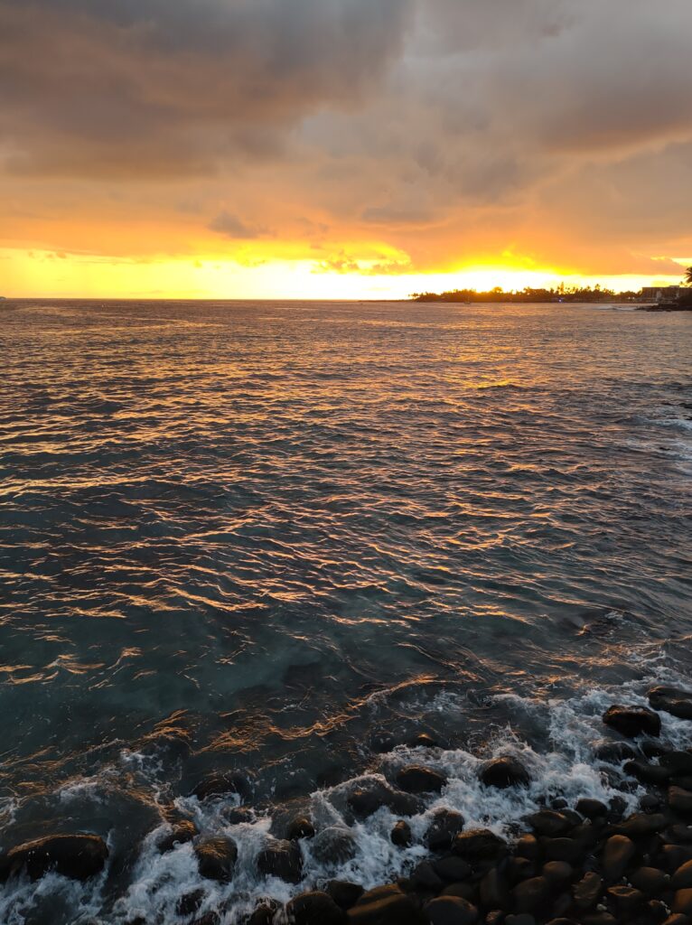Sunset sea view with golden sky reflecting on waves and smooth pebbles lining the shore wallpaper