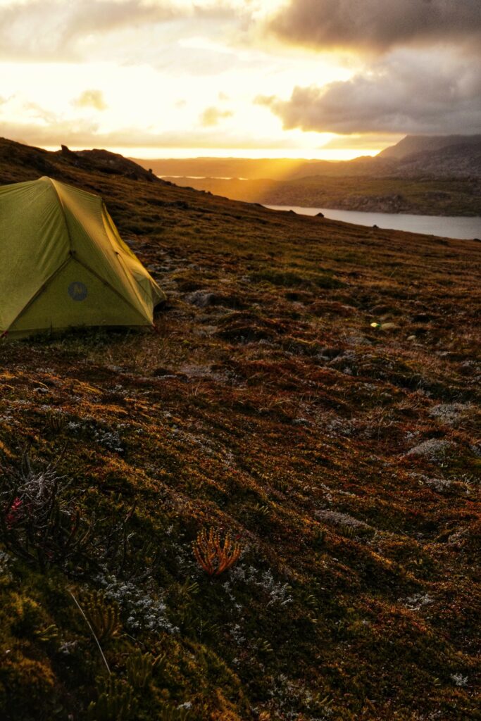 Solitary tent on rugged hill at golden sunset overlooking winding river dramatic sky nature scene Wallpaper