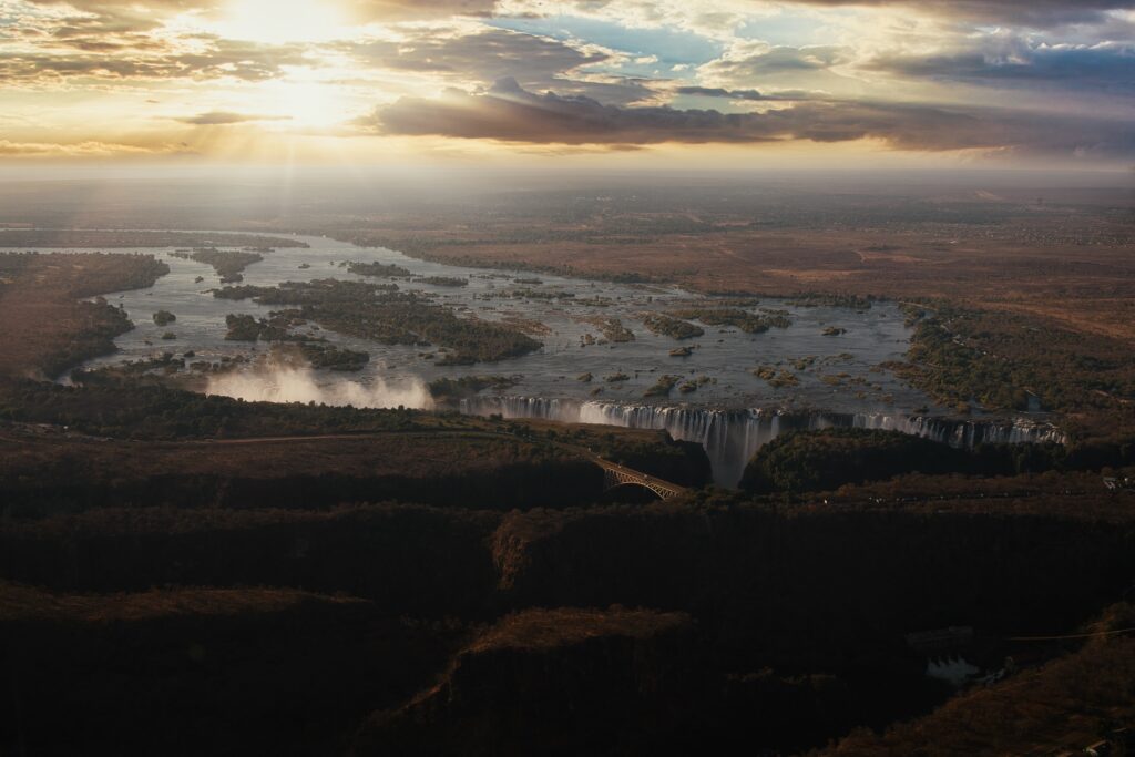 Breathtaking waterfall cascading from wide river through sunlit plain under golden sky Wallpaper