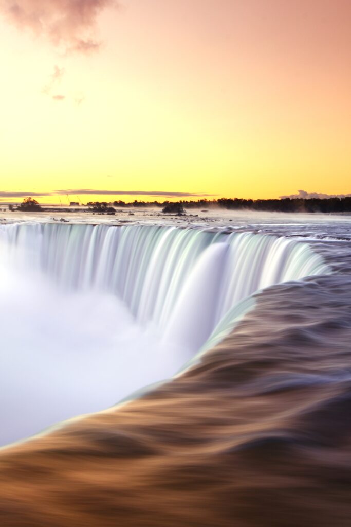 Waterfall cascading under golden sunset sky with smooth flowing streams and misty vibrant horizon Wallpaper