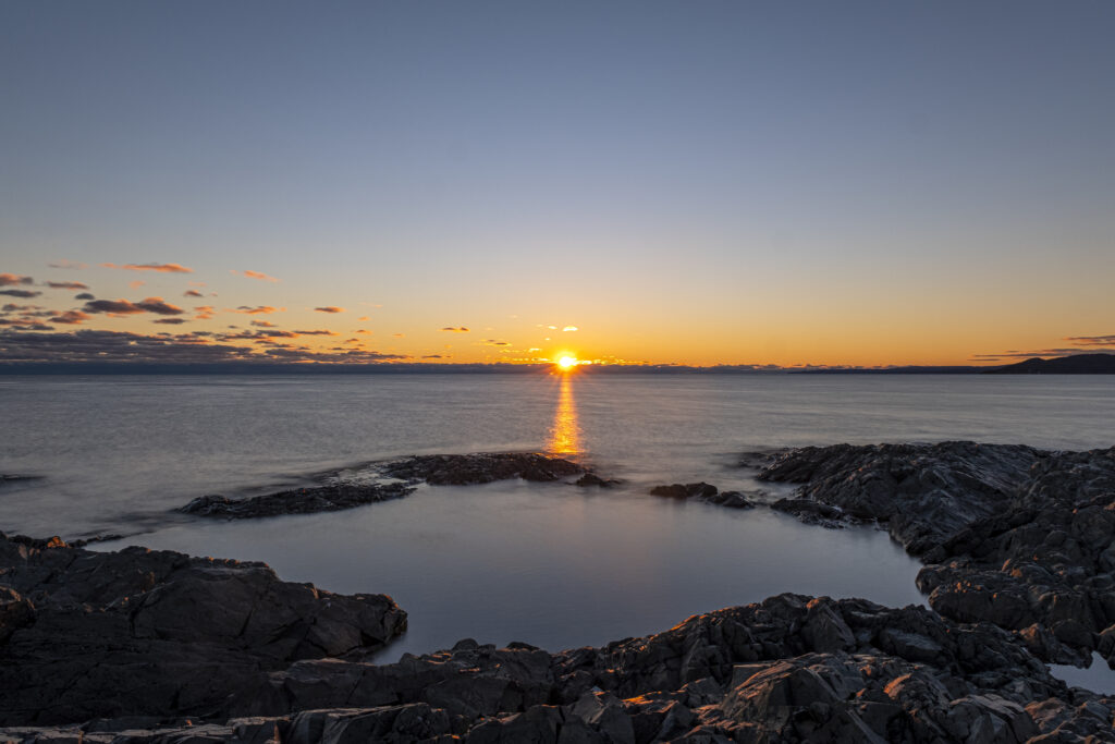 Serene sea sunset wallpaper with golden sun reflecting on calm water and rugged rocks