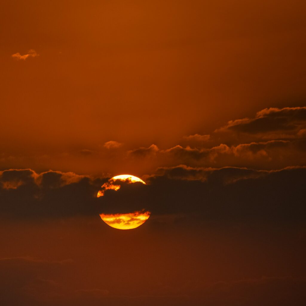 Striking sunset with glowing sun behind clouds in deep orange and golden hues wallpaper background