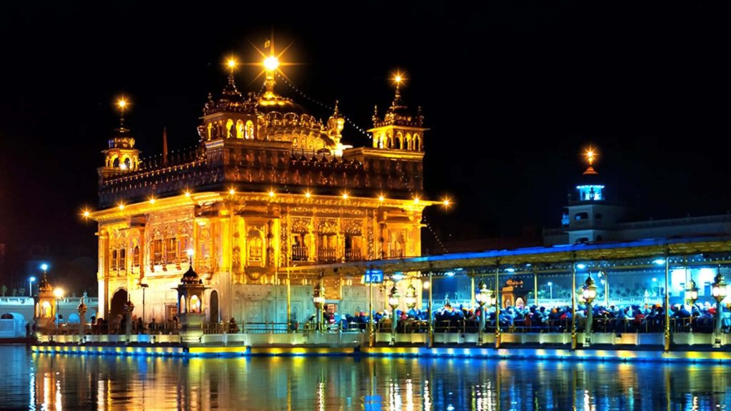 Golden Temple Amritsar glowing at night with golden reflections on calm Sarovar waters serene view Wallpaper