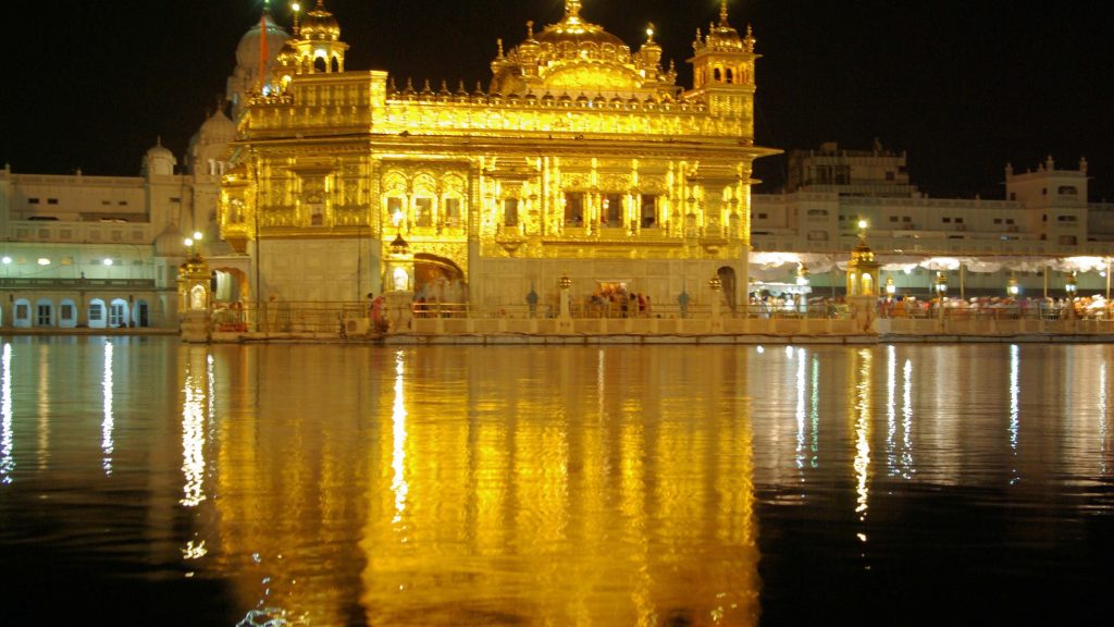 Golden Temple Amritsar glowing at night with clear reflection on calm holy pool water Wallpaper