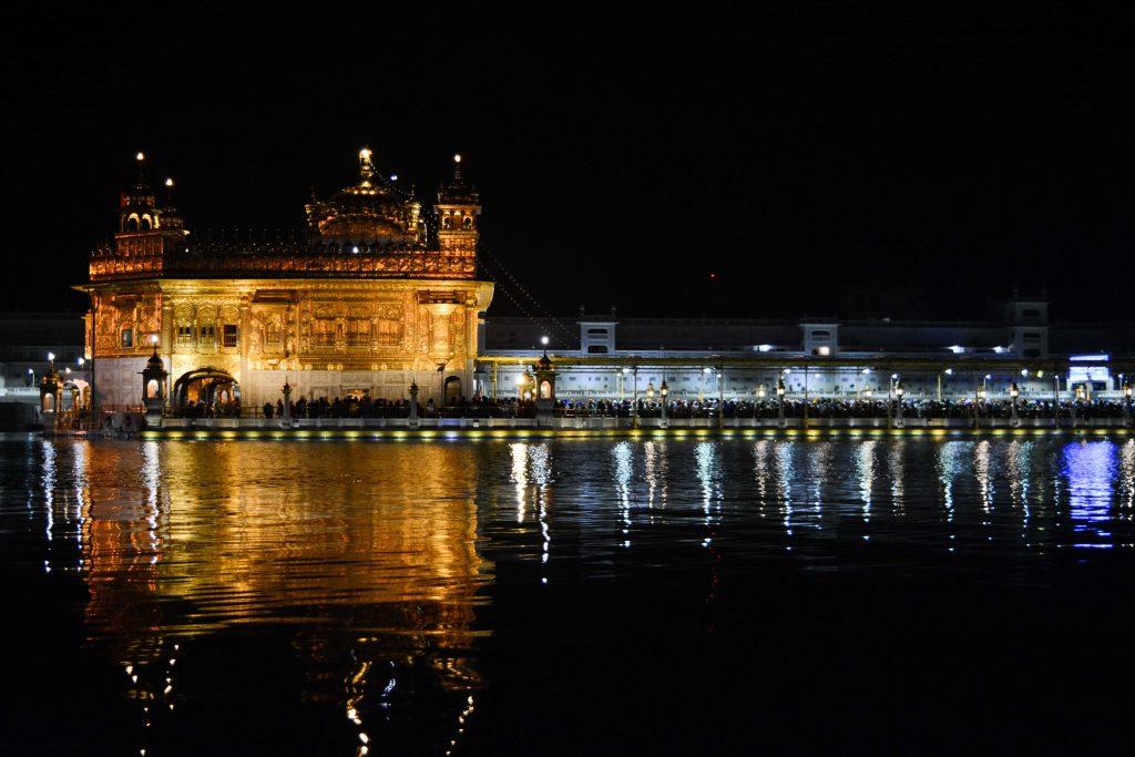 Golden Temple Amritsar glowing at night with vibrant reflections on calm sacred pool waters Wallpaper