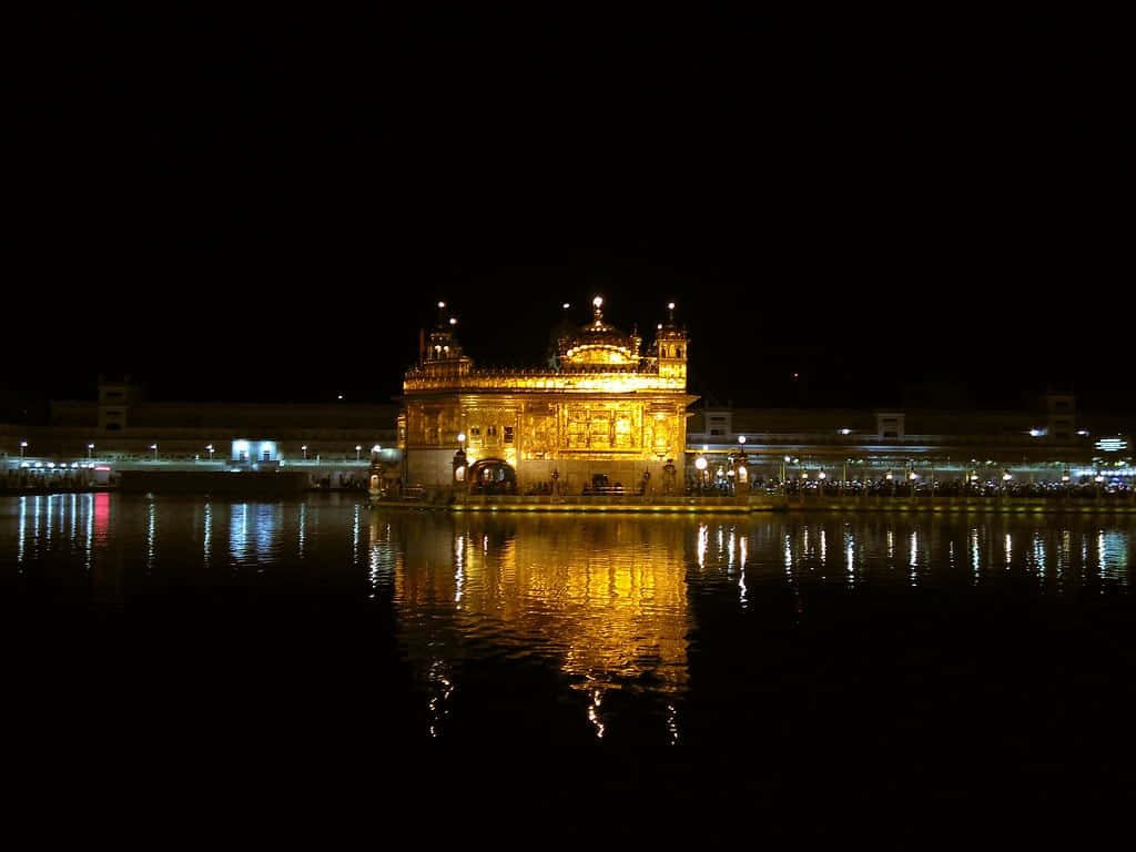 Golden Temple Amritsar illuminated at night reflecting on calm sacred pool water serene scene Wallpaper