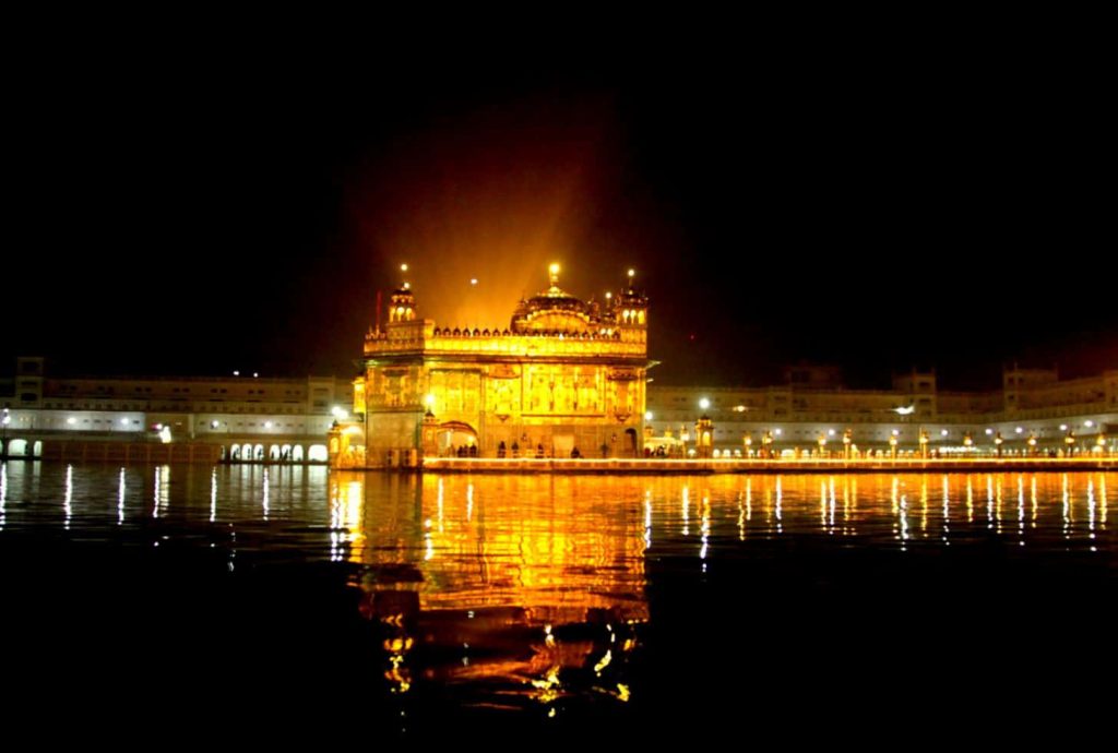 Golden Temple Amritsar glowing at night with shimmering reflection on calm water peaceful scene Wallpaper