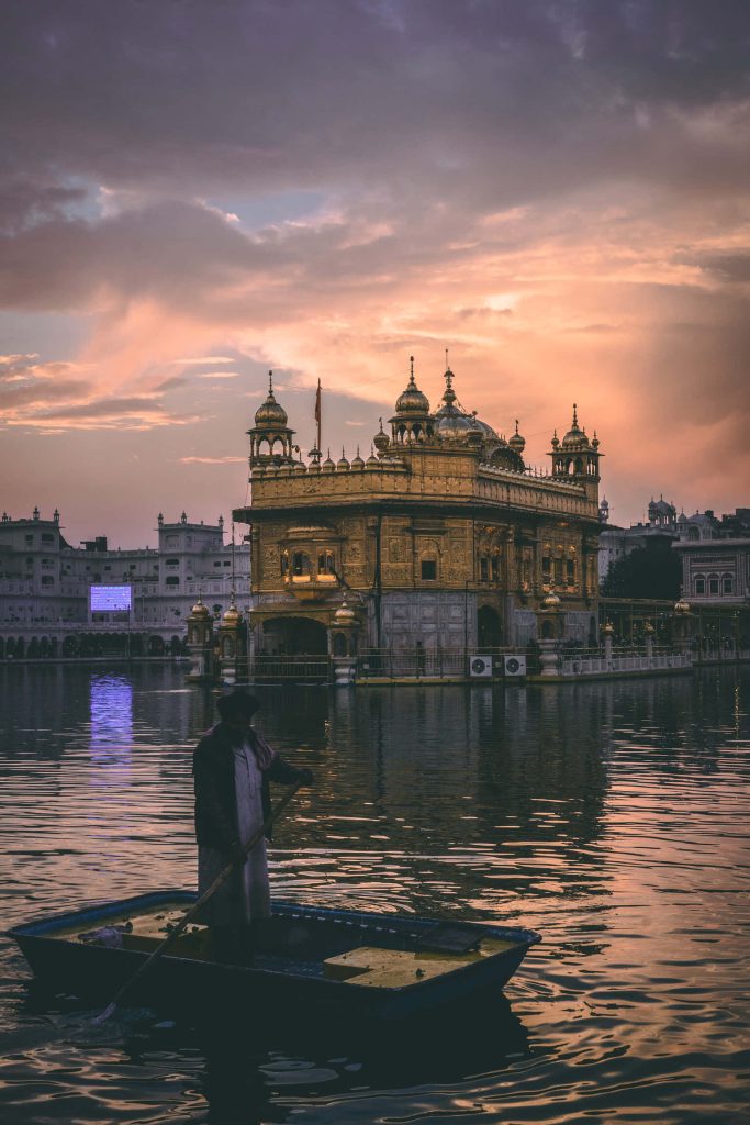 Golden Temple Amritsar at sunset with boatman on reflective sacred waters wallpaper background