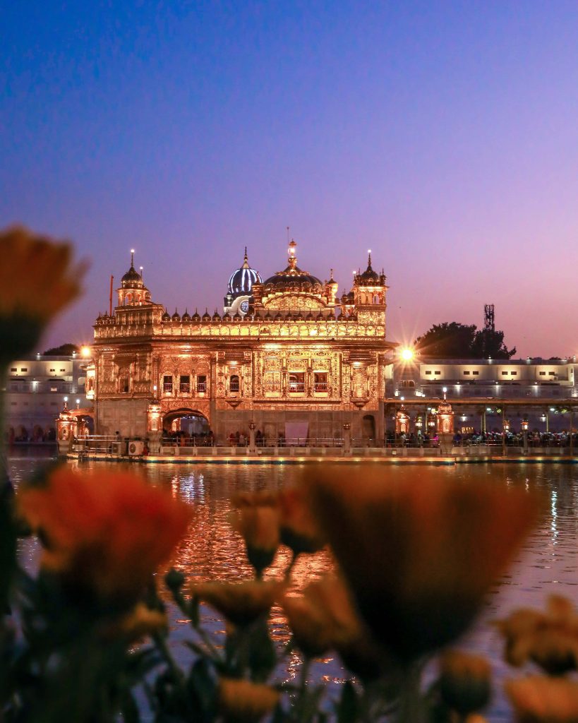 Golden Temple Amritsar glowing at twilight reflected in calm water with foreground flowers wallpaper