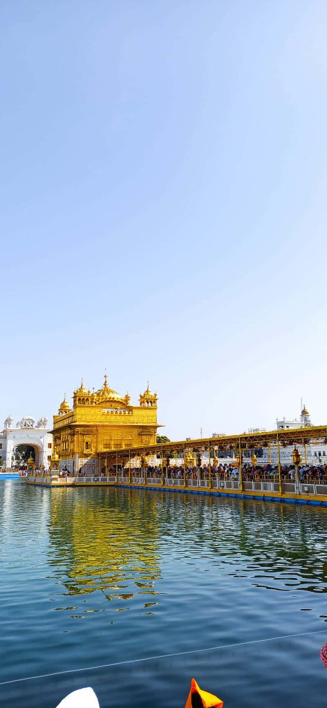 Golden Temple Amritsar sunlit with calm reflective waters and clear blue sky background wallpaper